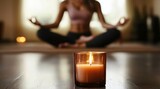 a lit candle with a girl in a yoga pose in the background