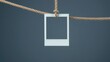 © Vibrant Visions Pixe - Blank instant photo frame hanging from rustic rope against a muted blue background.