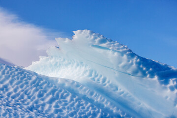 Wall Mural - jagged edge detail of a blue iceberg against blue sky and cloud background. kjerulf fjord, northeast