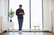 © sofiko14 - Young Indian man in casual attire using smartphone in modern office environment near large window with natural light.