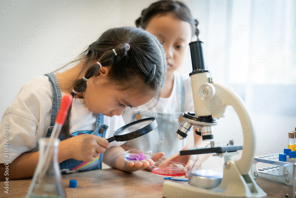 Two young girls are looking through a microscope at a slide. One of the ...