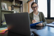 © Songsak C - Concentrated at work. Confident young woman in smart casual wear working on a laptop while sitting near a window in a creative office.