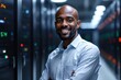 © ThomasLENNE - portrait of a smiling senior Sudanese male IT worker looking at the camera, against dark server room  background.