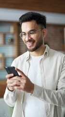 Handsome man using mobile phone sitting on sofa in living room at home. Male browses social networks, does shopping online, chats with friends, writes or reads messages. Close up. Vertical video