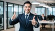 © Atif - A confident businessman in a suit smiles, thumbs up, standing confidently in his office