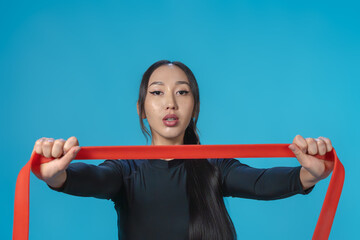 Wall Mural - Asian girl in sportswear training with rubber expander. Isolated blue background. Healthy lifestyle concept. Close-up