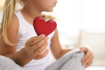 Wall Mural - Orphanage concept. Little girl with red heart figure indoors, closeup. Space for text