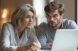 © Kevin - Two busy colleagues working together talking using laptop in office. Middle aged Latin female manager teaching young male worker looking at computer discussing business plan at office, Generative AI