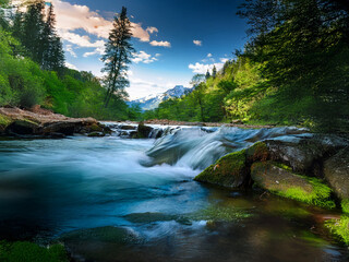 Poster - Serene mountain river flows over mossy rocks, lush green forests frame the vibrant scene under a dramatic sky.  Sunlight illuminates the cascading water.