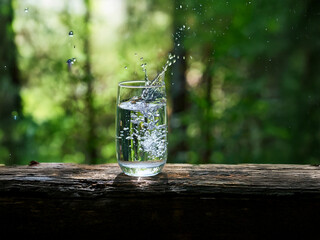 Poster - A glass of pure water splashes on a rustic wooden surface, set against a vibrant, sun-dappled forest backdrop.  The scene evokes freshness and tranquility.