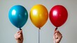 © hanif - Three hands holding colorful balloons; blue, yellow, and red.