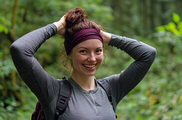 Wall Mural - A woman putting on her maroon headband while hiking in the forest during foggy weather, smiling and happy, wearing a gray shirt with black pants and a backpack