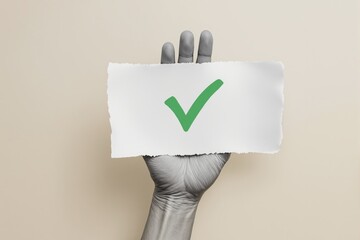 Poster - Hand holding torn paper with green check mark on bright beige background.
