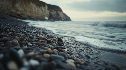 Wall Mural - coastal gravel pebbles on shoreline with gentle waves and scenic cliffs in background during dusk li