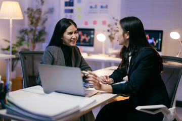 Aufkleber - Two young businesswomen are working together on a project in a modern office at night, discussing strategies and analyzing data on a laptop, demonstrating teamwork and dedication
