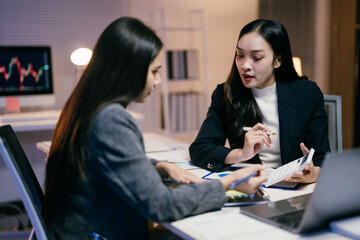Aufkleber - Two young businesswomen are working late in the office, analyzing financial charts and discussing investment strategies during a productive meeting
