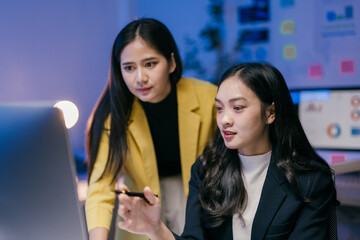 Aufkleber - Two young businesswomen collaborating on a computer in a modern office, discussing strategies and analyzing data late at night