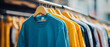© F-STUDIO - A vibrant display of colorful clothing hanging on wooden hangers in a retail setting, showcasing a mix of sweatshirts in various shades.