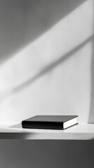 Wall Mural - A Minimalist Still Life: Black Book on a White Shelf, Capturing the Play of Light and Shadow on a Modern Interior Wall