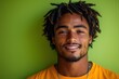 © Roman Ribaliov - Smiling young man with dreadlocks poses against a vibrant green background during daytime