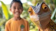 © VIK - A macro shot of a chameleon in the jungle captures a happy child's reaction to the green reptile. The big lizard is seen against the backdrop of a smiling kid, showcasing a wild animal in a tropical