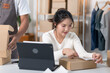 © snowing12 - A woman prepares a package for shipping, while another person scans a label in a workspace filled with boxes and clothing racks.