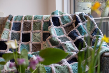 Old fashioned hand made crocheted wool blanket, throw, made up out of granny squares of different colours. Photographed thrown over a retro style sofa.