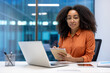 © Liubomir - Portrait of a serious business woman inside the office at her workplace, businesswoman looking at camera, working with a laptop, holding a notebook in hands, recording data from an online meeting