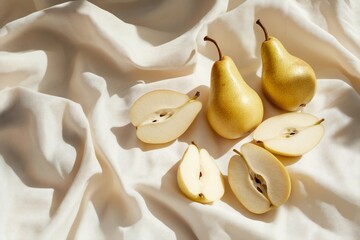 Poster - Two whole and four halved yellow pears arranged on a creamy fabric background, illuminated by sunlight.