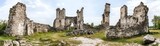 Ruins of an ancient castle surrounded by grass and trees under a cloudy sky.