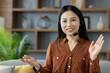 © Liubomir - Asian woman wearing headset smiling while engaged in virtual communication. Sitting in home environment. Concept of remote work and friendly customer service interaction.