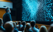 © Curioso.Photography - A professional speaker presenting a dynamic visual of interconnected glowing blue and orange networks to an engaged audience in a dark room.