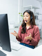 © kan - Portrait of Asian businesswoman, call center agent wearing headset giving support to customer at Virtual help desk in office. Young asian woman call center working at helpdesk for customer support.