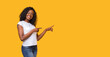 © Prostock-studio - Cheerful black lady in white t-shirt pointing at copy space on yellow studio background. Smiling african american young woman showing exciting advertisement or announcement, panorama with empty space