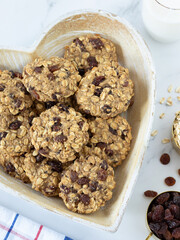 Wall Mural - Oatmeal raisin cookies in a heart shape plate with a glass of milk on white marble table. Top view.