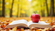 © LunaStar - Red apple on open book among autumn leaves in a park, seasonal beauty