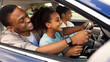 © Prostock-studio - Happy Black Father Teaching Daughter Driving Sitting Together. Kid Girl Learning To Drive Auto Having A Ride With Family In Urban Area. Automobile Ownership Concept. Side View