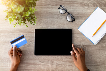 Poster - Top view of Afro lady with credit card using tablet pc for online shopping at wooden table, mockup for website or app. Millennial black woman ordering goods on touch pad, making contactless payment