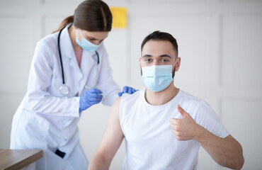 Poster - Get vaccinated. Young Caucasian guy showing thumbs up during coronavirus vaccination at clinic, promoting covid-19 immunization. Protection against global virus concept