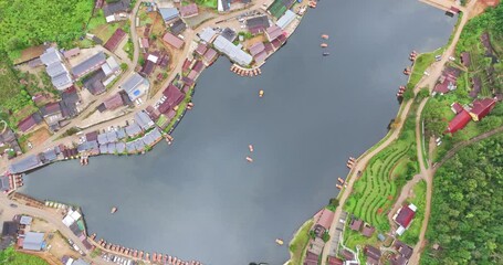 Wall Mural - aerial top view of a lakeside village, showcasing a mix of rustic architecture, lush greenery, and boats scattered across the calm water. A harmonious blend of natural beauty and human settlement.