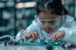 © Jane_S - Kid investors Day. Focused girl wearing safety goggles working intently on electronics in a high-tech lab environment.