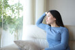 © PheelingsMedia - Relaxed asian woman sitting on a couch looking through a window