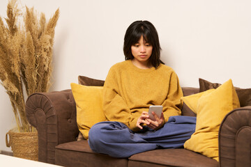 Young asian woman using smartphone on comfortable sofa at home