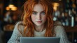 © Danila - A red-haired woman focuses on her laptop in a warm, cozy cafe, either studying or working remotely