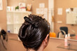 © AlbertoRodriguez - A woman with her hair in a ponytail is getting her hair done at a salon. The stylist is applying a product to her hair, and there are several bottles and a cup on the table. The salon has a mirror