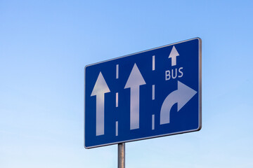 traffic sign with lane directions for cars and buses, featuring arrows and a bus lane symbol against a clear blue sky