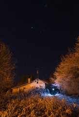 Wall Mural - Abandoned old house lit by a light with freeze trees and grass under night starry night sky. Astronomy background