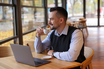 Man with cup of coffee working at table in cafe