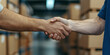 © DOUGLAS - close up of two people shaking hands in warehouse, symbolizing partnership and agreement, with cardboard boxes in background