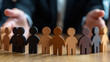 © Gabriele - Hands surrounding a row of diverse wooden figurines on a wooden table symbolizing protection, diversity, inclusion, and equality, representation of leadership and teamwork in human resources